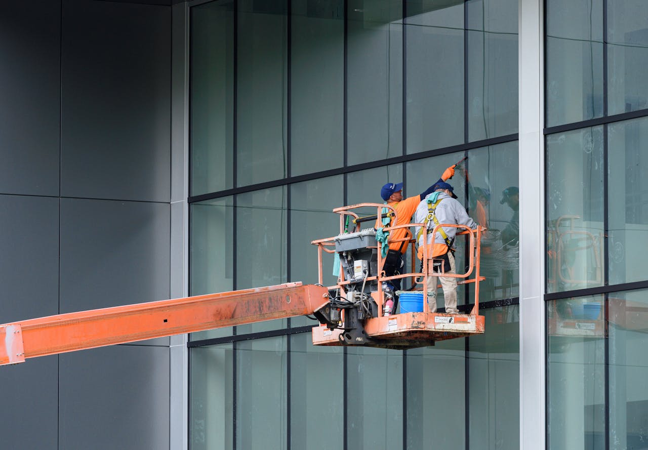 Workers on a lift platform cleaning glass windows of a modern high-rise building safely.