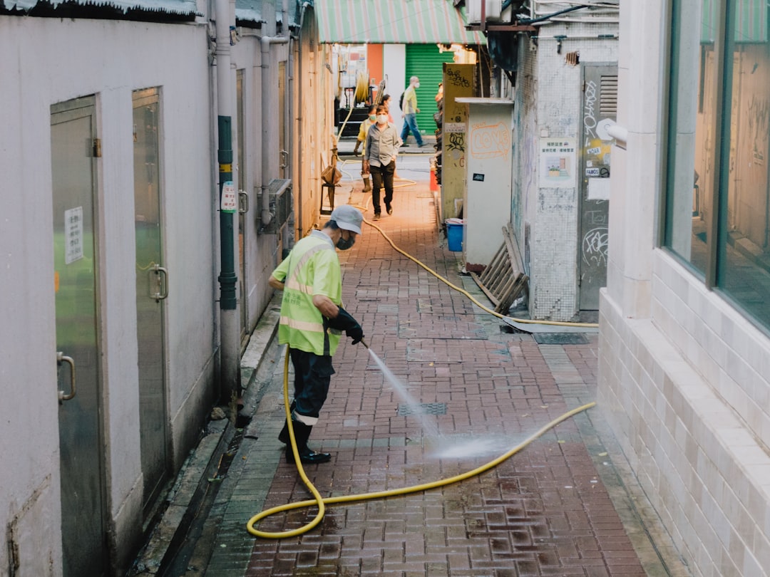 a-person-in-a-safety-vest-working-on-a-hose-in-a-narrow-alley-fuzxmqbixnc